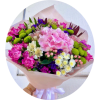 Handheld bouquet of pink, green, white, and purple flowers wrapped in pale paper