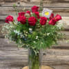 Red roses arranged in a tall glass vase with mixed greenery