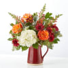 Mixed bouquet of orange, white, and red flowers in a red pitcher vase