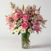 Pink roses and lilies arranged in a clear glass vase with white daisies