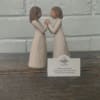 Two small figurines of girls facing each other and holding hands