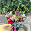 Colorful mixed flower arrangement in a black hatbox with a pink ribbon
