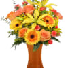 Orange roses and yellow lilies in a tall amber vase
