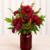 Red and purple chrysanthemum arrangement in a burgundy glass jar