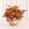 Orange and burgundy floral arrangement in a gold pumpkin container with plaid ribbon