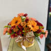 Orange and red mixed flowers arranged in a wooden basket with a patterned bow