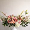 Delicate pink lilies and ranunculus bloom among clusters of peach roses, airy