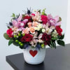 Mixed pink and red flower arrangement in a white pot with a red heart