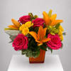 Bouquet of pink roses, yellow spray roses, and orange lilies in an amber vase