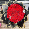 Round bouquet of red roses wrapped in black paper with gold trim