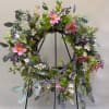 Floral wreath with pink daisy-like flowers and purple berries on a black stand