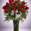 Red roses arranged in a tall glass vase with white filler flowers