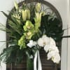 Tall floral arrangement with white orchids and green lilies in a vase