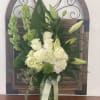 White roses and lilies arranged in a green vase with a ribbon