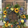 Floral wreath with sunflowers, blue blooms, and yellow carnations on a wooden shutter