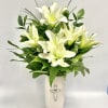 White lilies arranged in a white vase with green foliage
