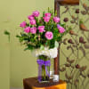 Pink roses in a clear glass vase with white flowers and a purple ribbon