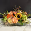 Mixed floral arrangement with peach roses and a sunflower in a low rectangular vase