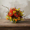 Bright orange and yellow floral arrangement with branch accents in a low bowl