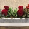 Four red roses with succulents in a ceramic planter wrapped in crystals.