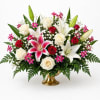 Mixed bouquet of white lilies, roses, and pink accent flowers in a gold vase