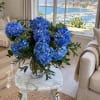 Blue hydrangea bouquet in a clear glass vase on a marble table