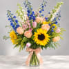 Mixed bouquet with sunflowers, roses, tulips, and blue flowers in a glass vase