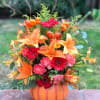 Autumn floral arrangement in a pumpkin-shaped container with orange lilies and red daisies