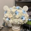 White floral arrangement with blue orchid accents on a textured stand