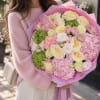 Woman holding a large pink and cream bouquet with green hydrangeas