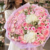 Woman holding a large bouquet of pink and white flowers wrapped in lavender paper