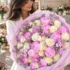 Woman holding a large bouquet of pink and cream flowers wrapped in pastel paper