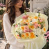 Woman holding a large pastel bouquet of roses and carnations wrapped in pale paper