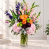 Mixed bouquet of orange roses, pink hydrangeas, and purple flowers in a clear glass vase