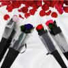 Four single roses wrapped in black sleeves with rose petals scattered above