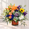 Mixed bouquet with orange lilies, roses, sunflowers, and purple flowers in a glass vase
