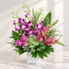 Pink and purple orchid arrangement in a white square vase