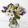 White lilies and daisies with purple filler in a clear glass vase