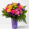 Mixed bouquet of orange roses, pink daisies, and purple filler in a purple vase