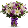 Lavender roses and white lilies in a glass vase with a purple ribbon