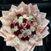 Bouquet of red, pink, and white roses wrapped in blush paper with pearl accents