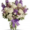 White roses and purple flowers in a glass vase with a purple ribbon
