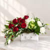 Red roses and white flowers arranged in a white suitcase-style container