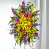 Tall standing floral spray with yellow lilies, orange roses, and purple flowers