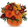 Autumn floral arrangement in a pumpkin-shaped container with orange and burgundy blooms