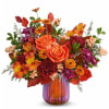 Orange roses and mixed autumn flowers in a striped glass vase