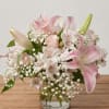 Pink lilies and white filler flowers arranged in a clear glass vase