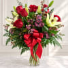 Red roses and white lilies in a clear glass vase with a red ribbon
