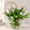 Pink tulips arranged in a clear glass bowl vase with curly branches