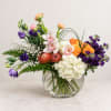 Mixed bouquet of orchids, roses, hydrangea, and purple blooms in a glass vase